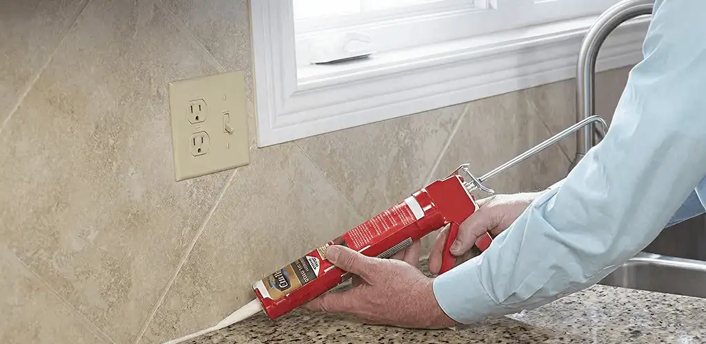 Handyman applying caulk along a kitchen backsplash and countertop seam in New Haven, CT